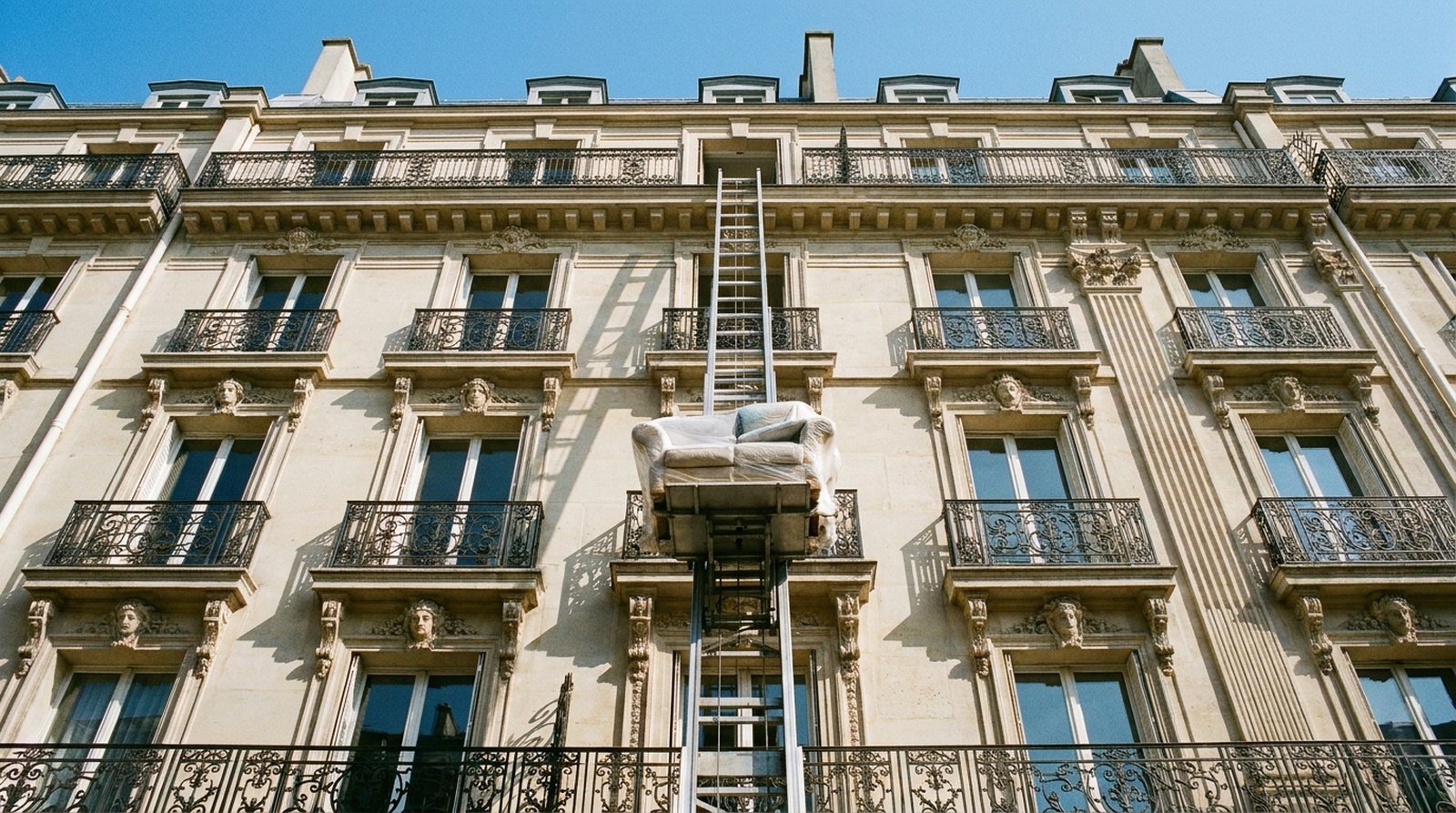 Monte-meuble déployé sur une façade haussmannienne, canapé housse en cours de descente.